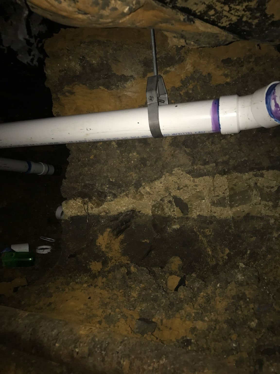 White PVC pipe secured to a dark, rough stone wall with a black strap in a dim, enclosed space.