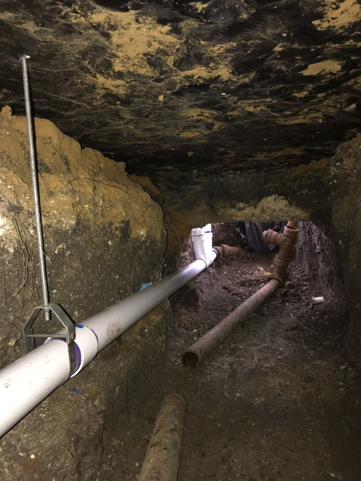 Narrow trench with white PVC pipes and dirt walls. Brown pipes run alongside.