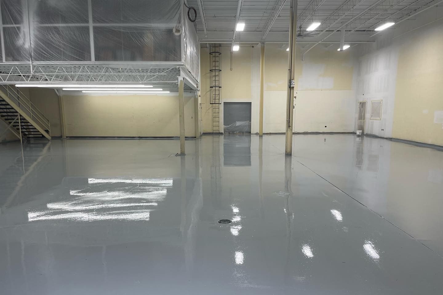 A large empty warehouse with a gray floor and stairs.