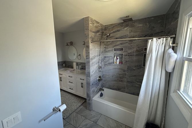 A bathroom with a tub , shower , sink and mirror.