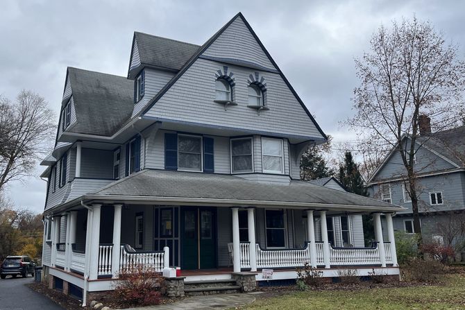 A large white house with a large porch on a cloudy day.