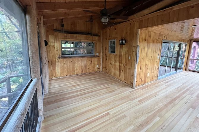 A screened in porch with wooden floors and a ceiling fan.
