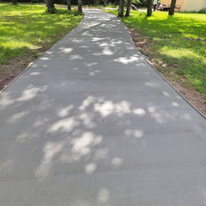 A concrete walkway going through a park with trees on both sides.