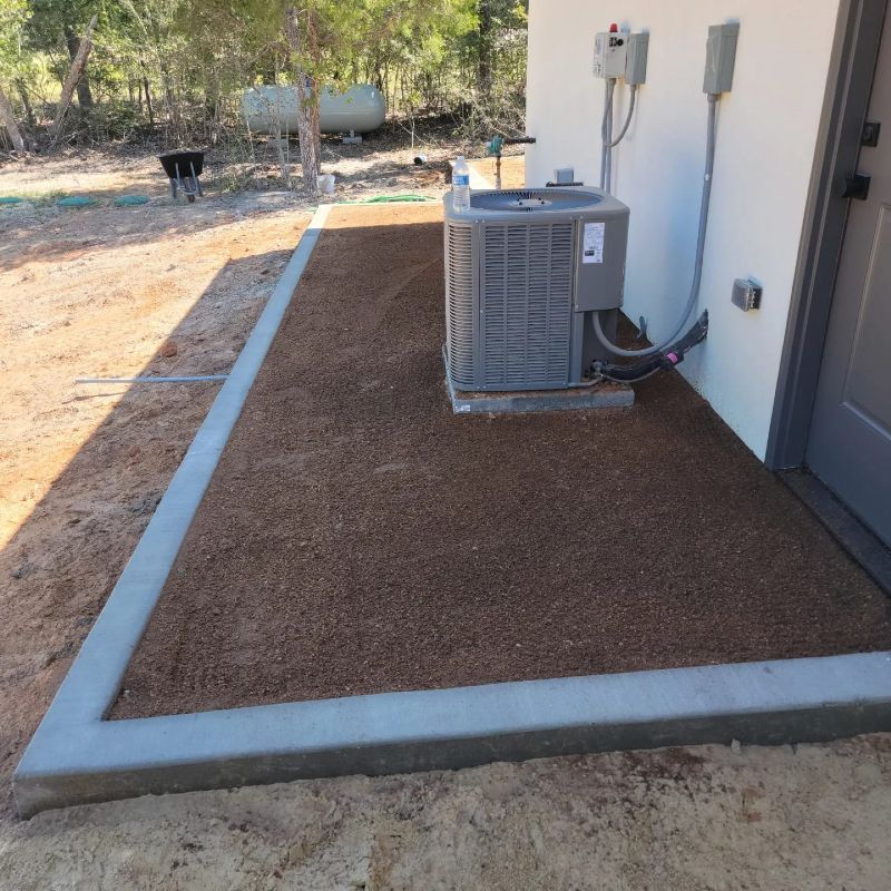 A gray air conditioner is sitting in the dirt next to a white building