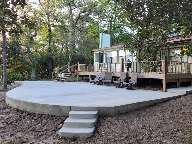 A concrete patio with stairs leading to a wooden deck in front of a house.