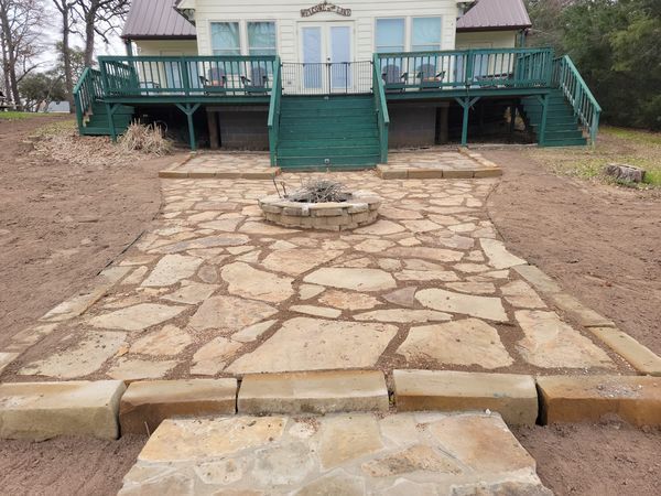 A stone walkway leading to a house with a fire pit in front of it.