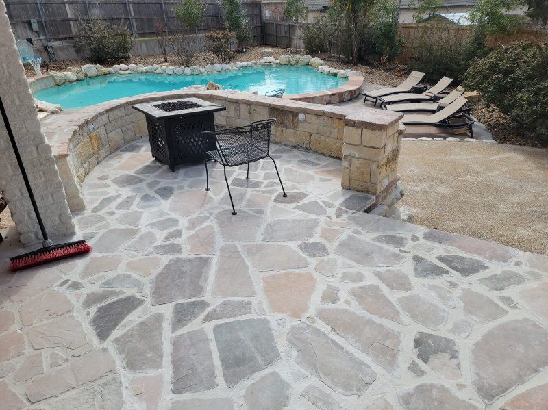 A patio with a fire pit and chairs next to a pool.