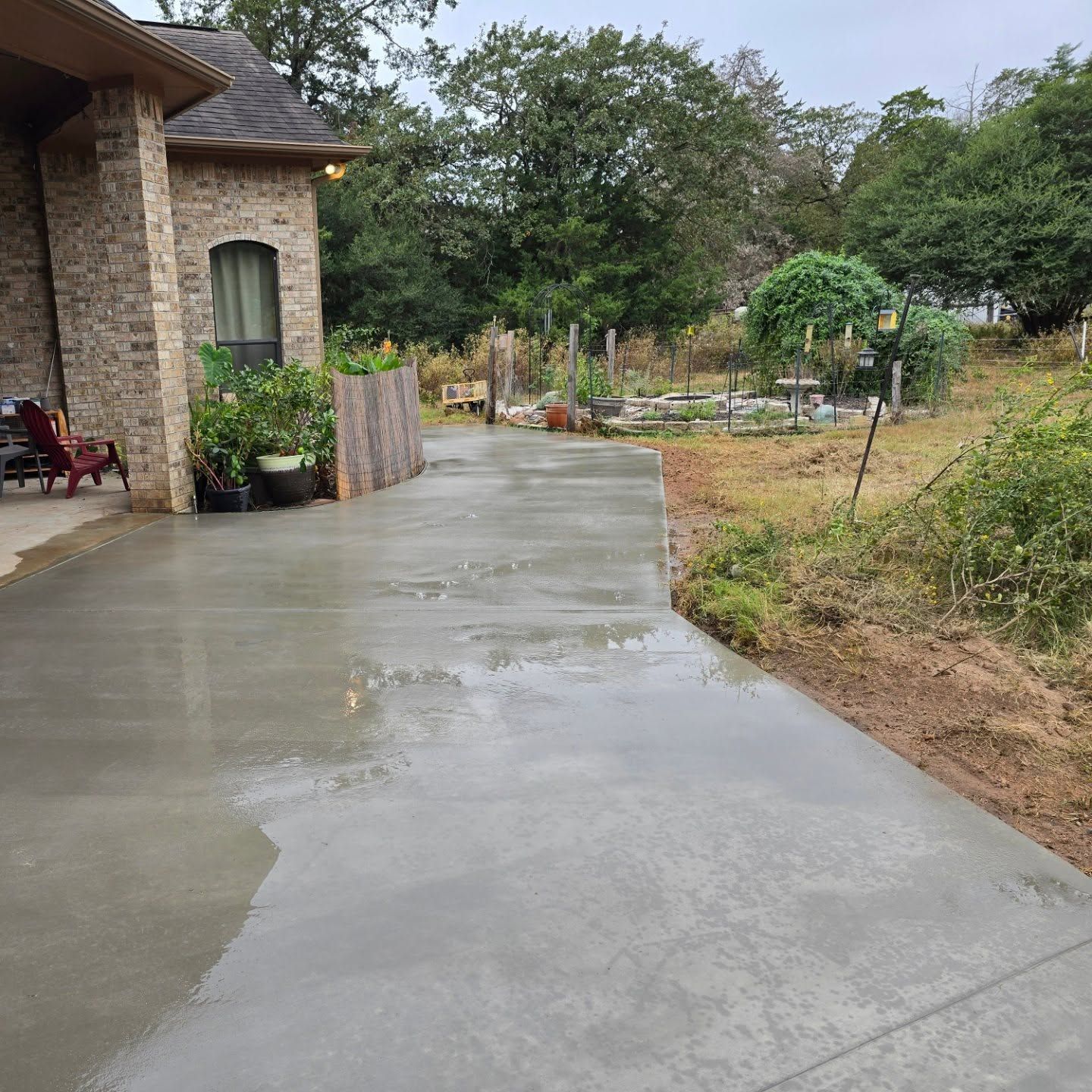 A concrete driveway leading to a house with a brick building in the background.
