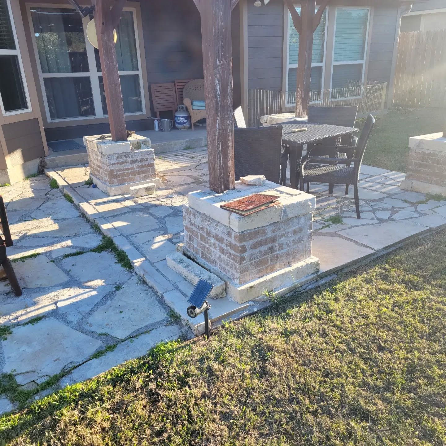 A patio with a table and chairs under a pergola in the backyard of a house.
