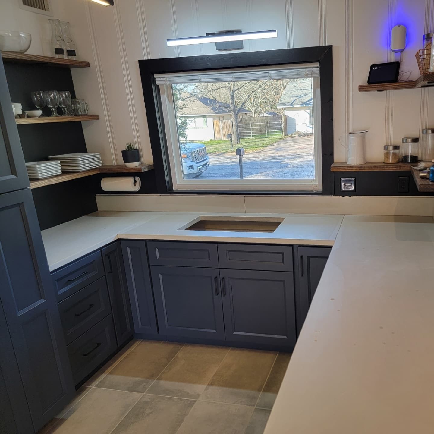 A kitchen with blue cabinets and white counter tops and a window
