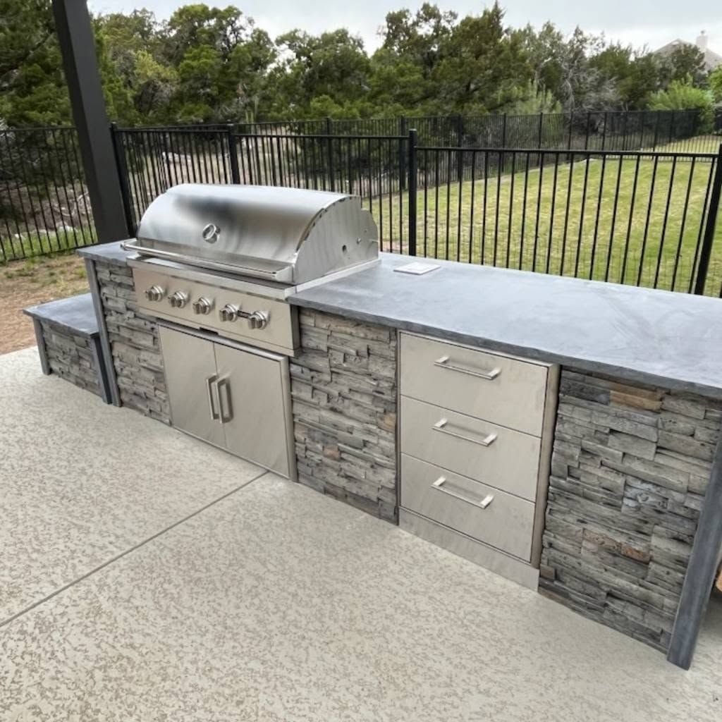A large outdoor kitchen with a grill and a fence in the background.