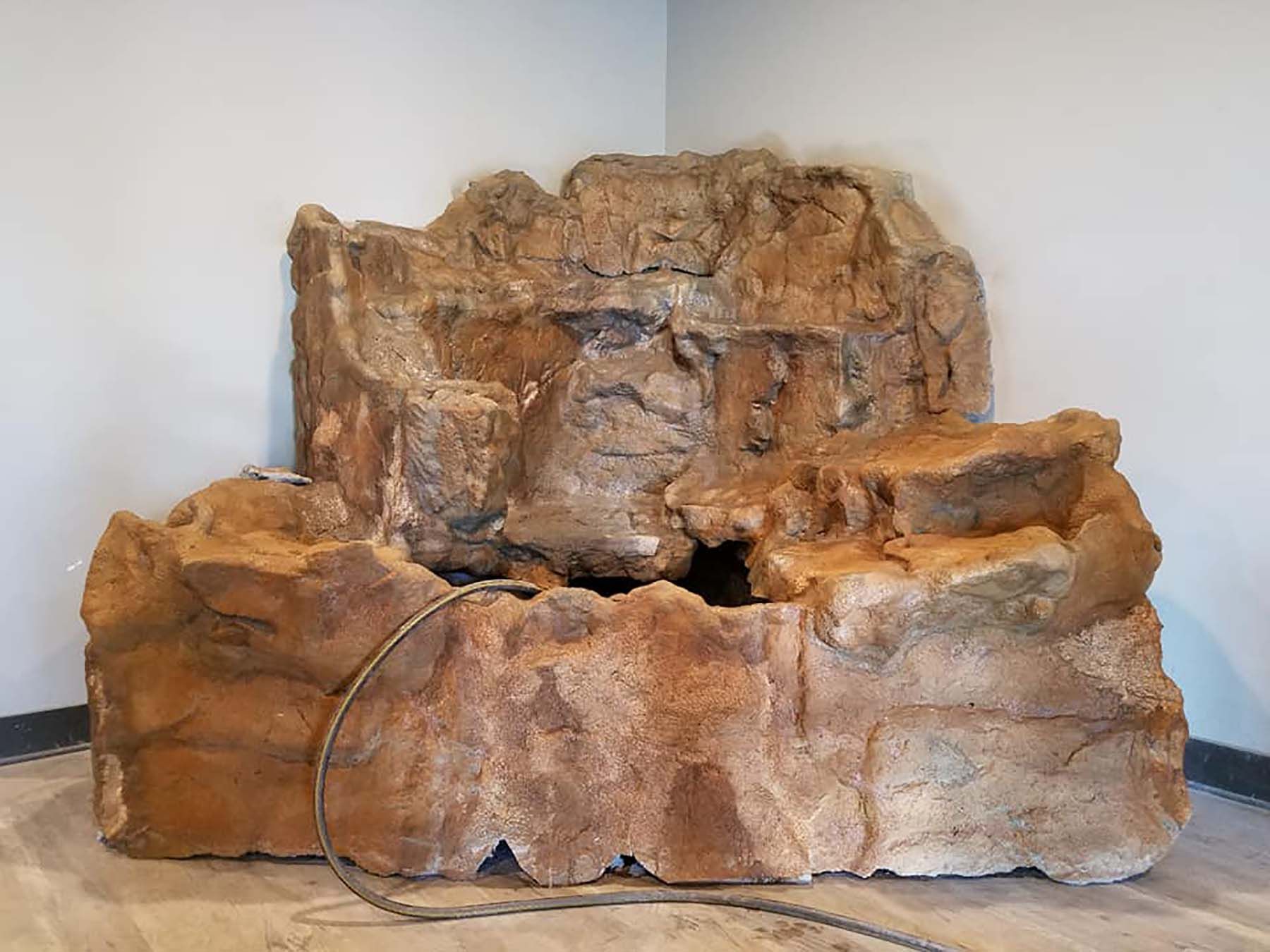 A large rock with a hose attached to it is sitting in a corner of a room.