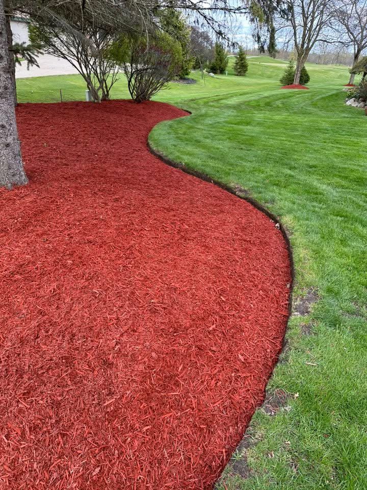 A lawn with red mulch and a tree in the background.