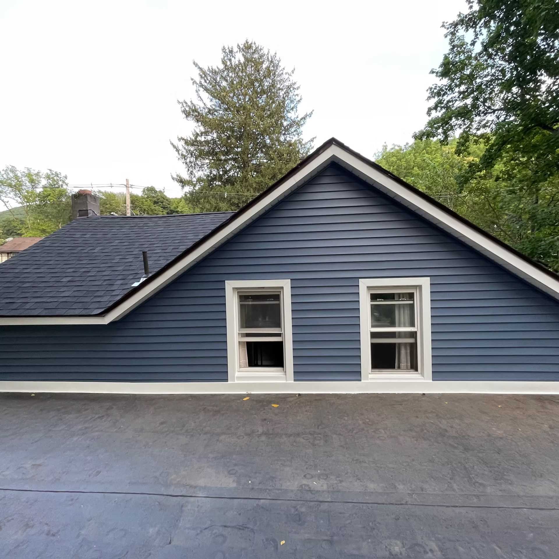 Blue house siding with two windows and dark roof.