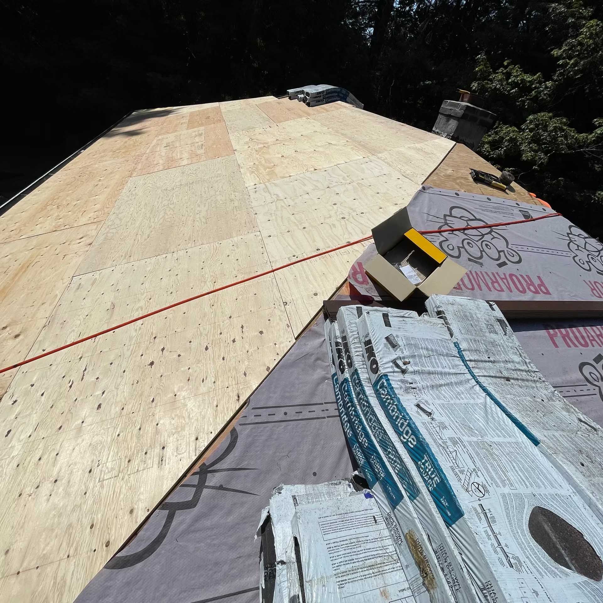 Roof under construction, plywood and roofing materials visible.