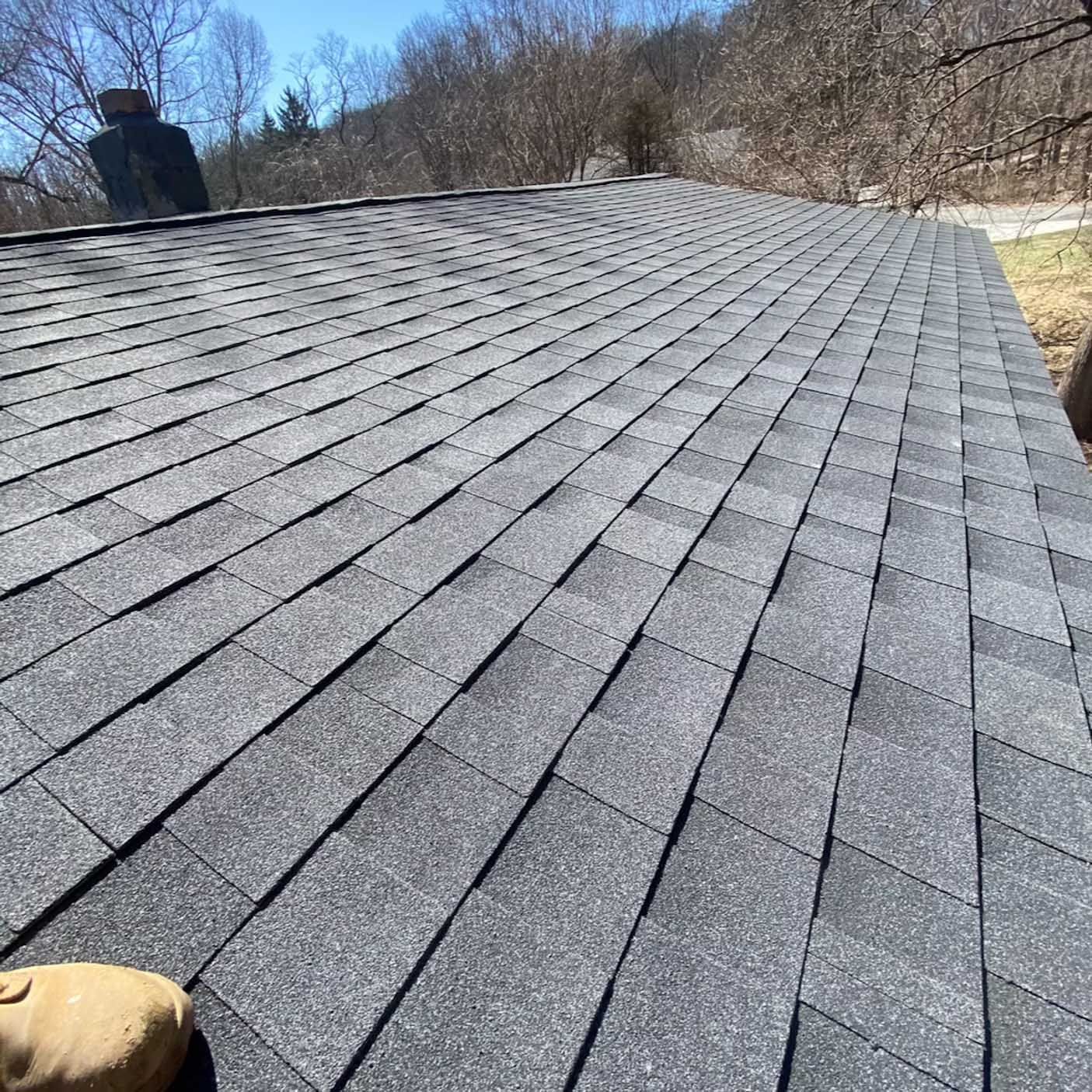 Gray asphalt shingle roof with some trees in the background on a sunny day.