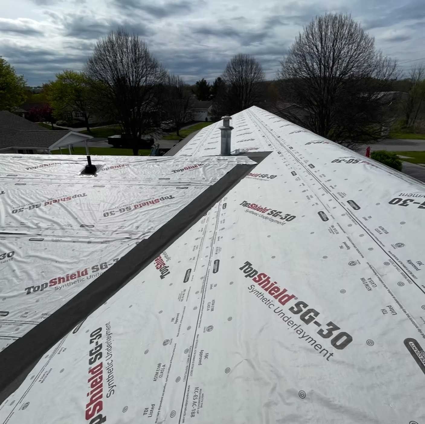 Rooftop with protective underlayment. Chimney and vent visible against a cloudy sky.