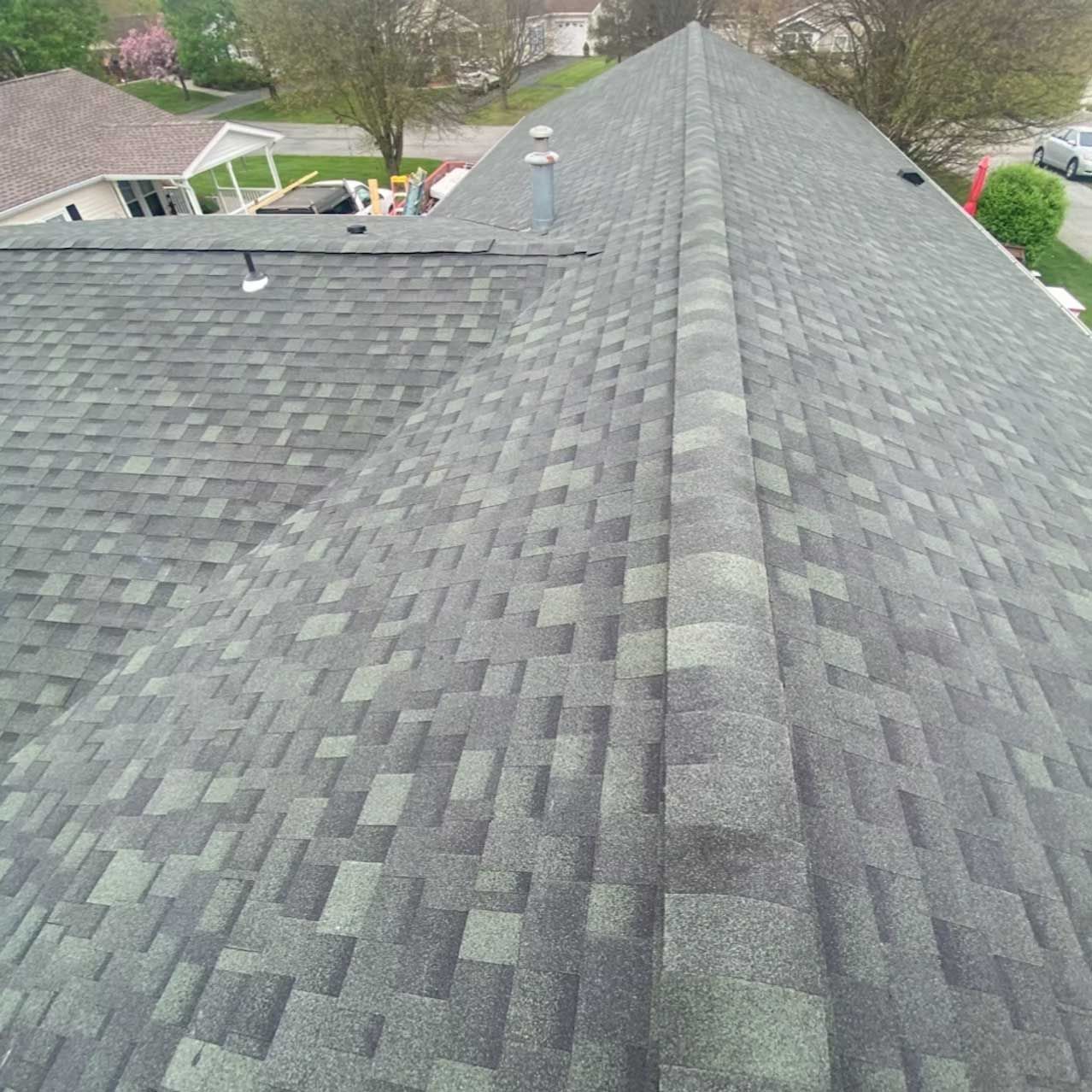 Overhead view of a gray asphalt shingle roof on a residential house with a central ridge.