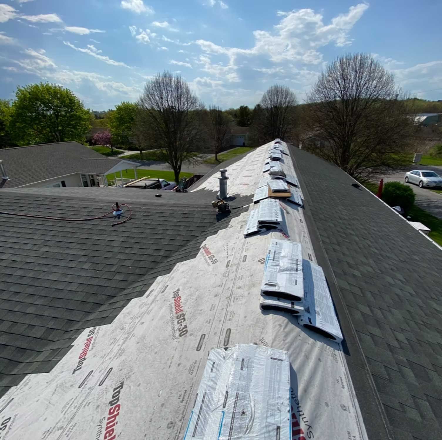 Roofer working on a partially shingled roof. Underlayment, new shingles, and supplies visible on a sunny day.