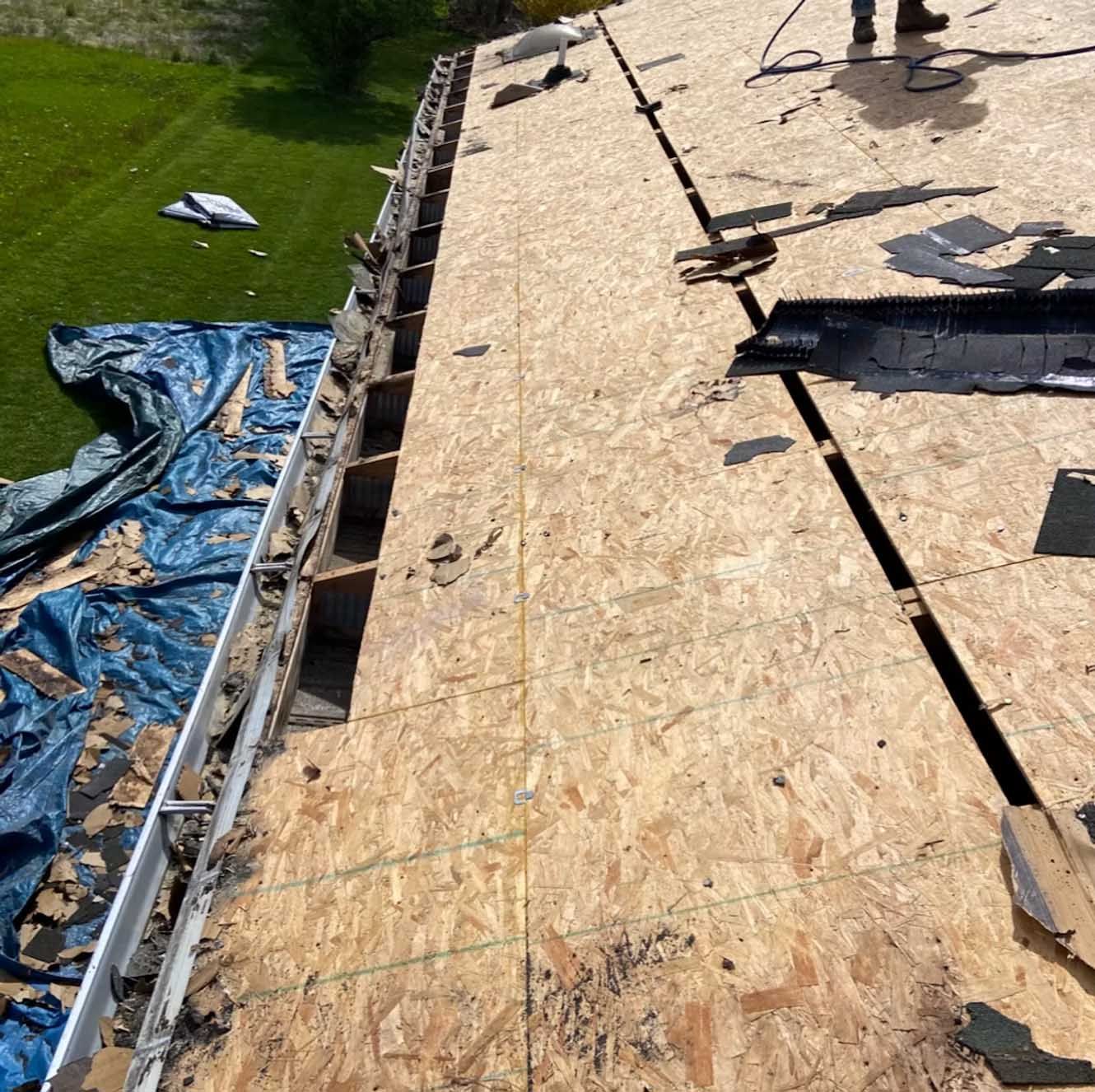 Rooftop undergoing repair, with exposed wood, gutter, and protective tarp; person visible in upper right.