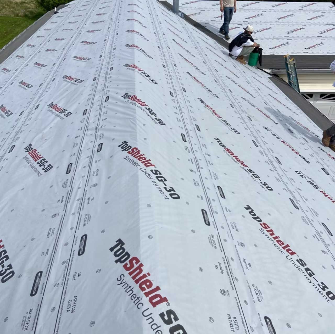 Workers installing TopShield SG-30 synthetic underlayment on a roof.