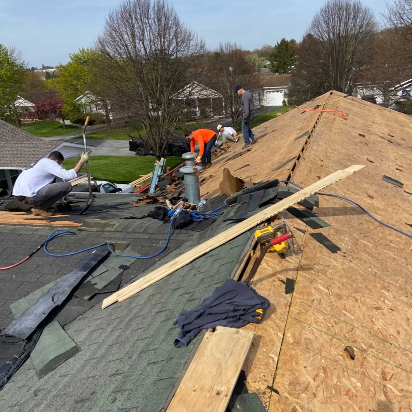 Roofers replacing shingles on a residential roof, using tools and working in the sunlight.