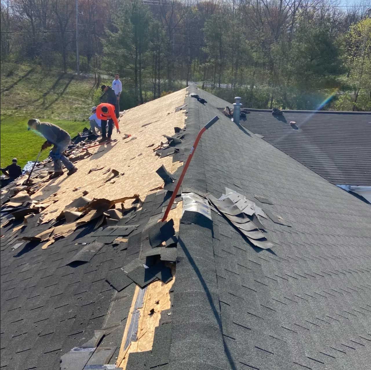 Roofers removing old shingles from a house roof on a sunny day.