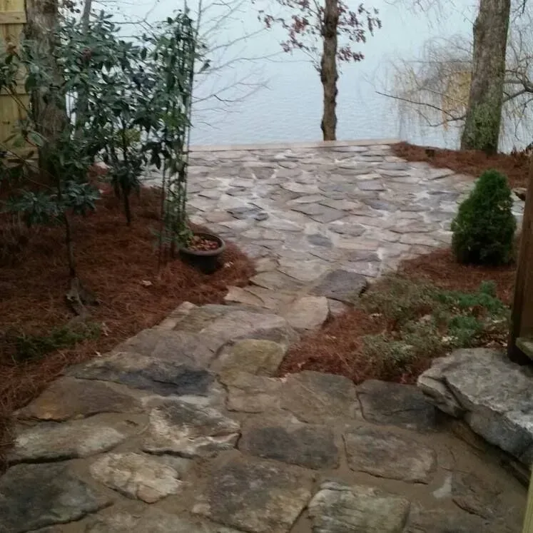 Stone pathway leading through a small garden toward a misty lake, with shrubs and trees on both sides