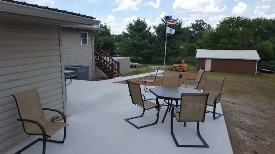 Patio with table and chairs beside a house, overlooking a yard and small shed under a partly cloudy sky