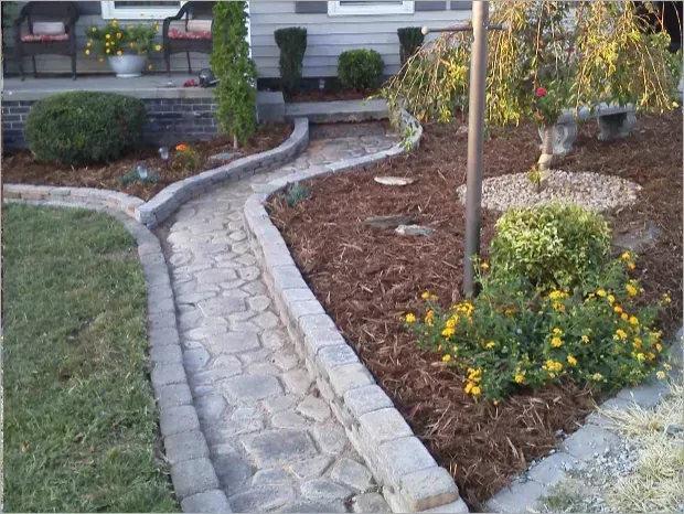 Curved stone garden path beside mulch beds, shrubs, and yellow flowers in a landscaped yard