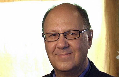 A bald man wearing glasses and a suit is smiling for the camera.