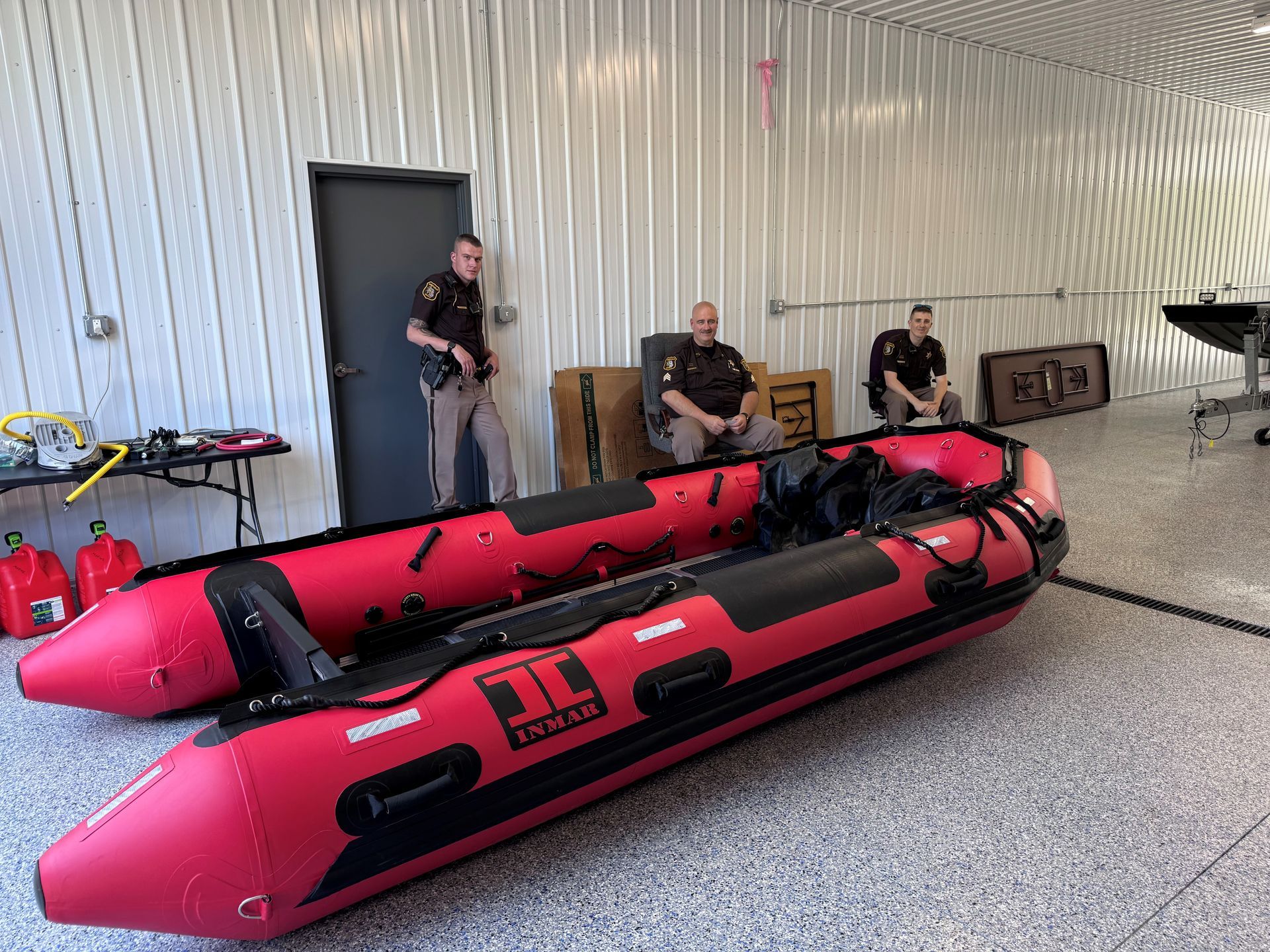 Two red inflatable boats sit inside a building with three uniformed officers.