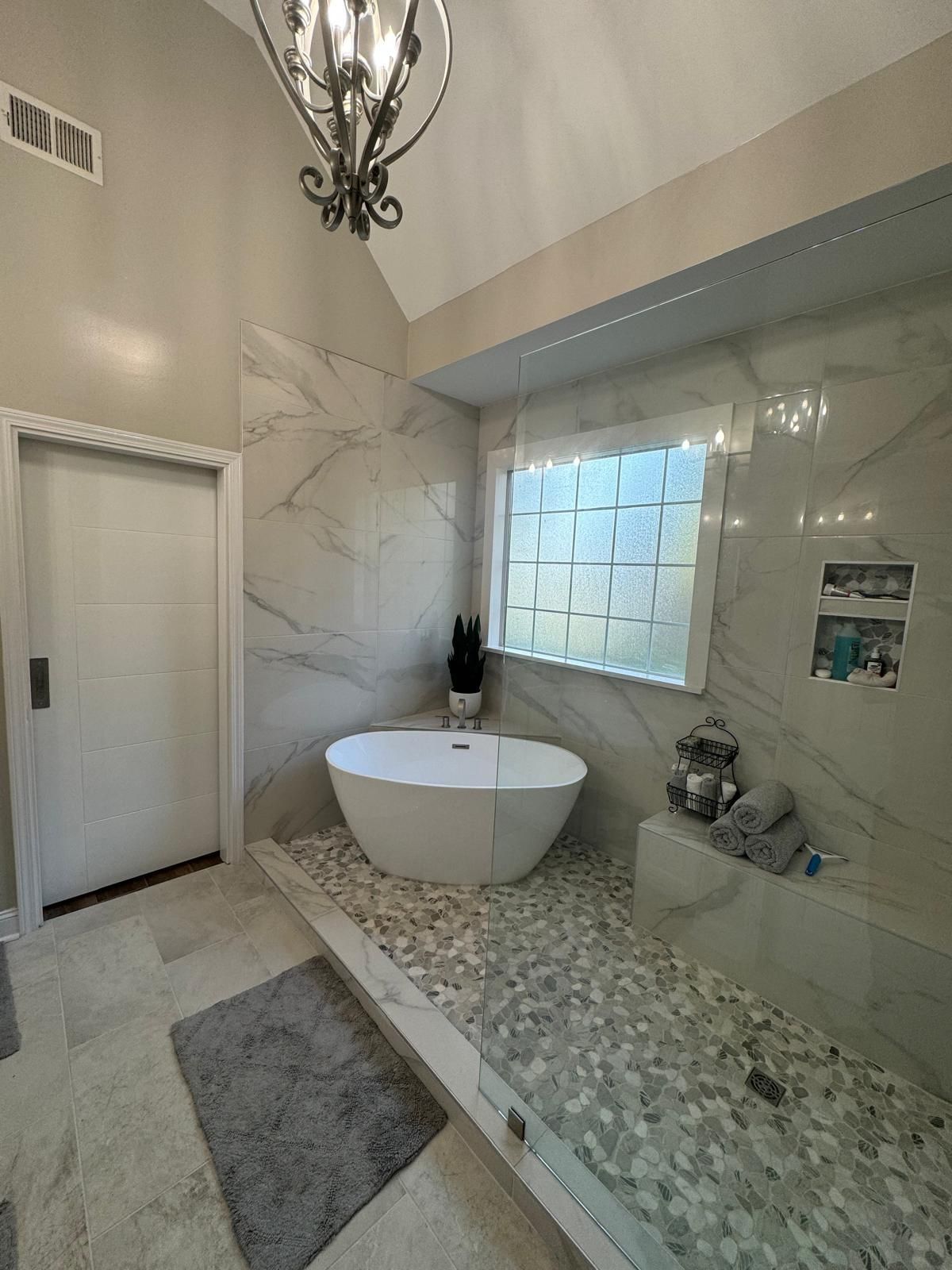 Modern bathroom with a freestanding tub, pebble floor, and marble walls.