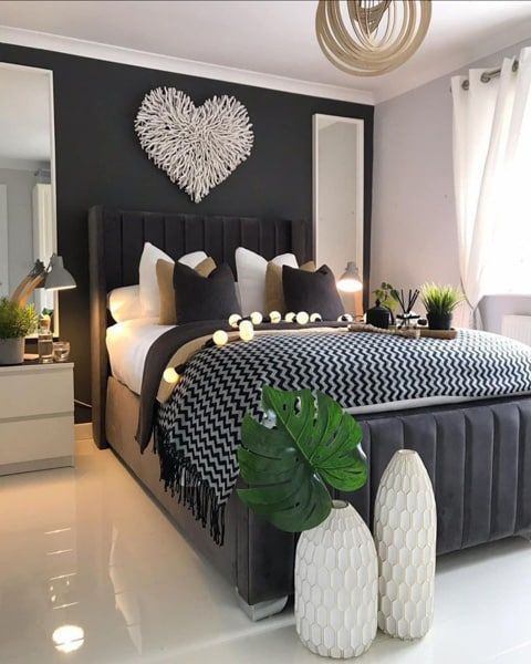 Cozy bedroom with a gray bed, white vases, and a heart-shaped wall decor against a dark wall.