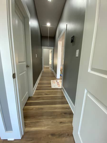 Long hallway with grey walls, white doors, and wood-look flooring.