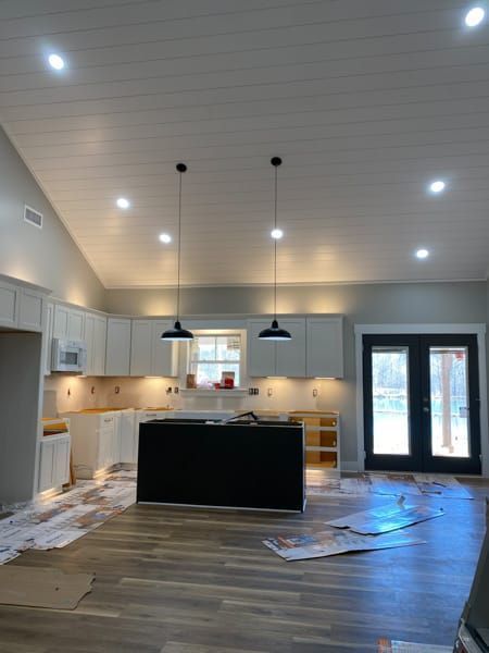 Kitchen with white cabinets, black island, black pendant lights, and wooden flooring.