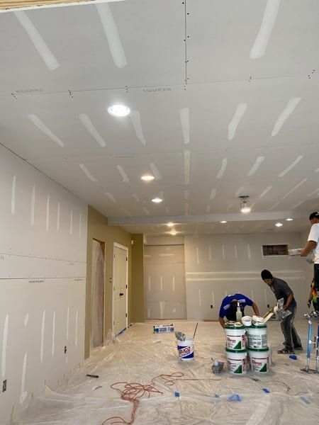 Construction workers apply mud and tape to drywall ceiling and walls.