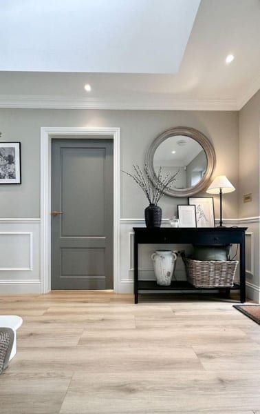 Gray door, black console table with mirror and basket. Light wood floor, white trim.