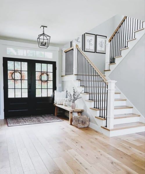Bright entryway with black double doors, a wooden bench, staircase, and light wood flooring.