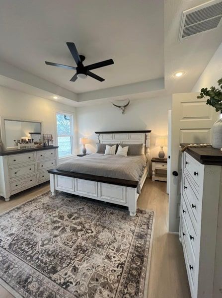 Spacious bedroom with white and brown furniture, a large patterned rug, and a black ceiling fan.