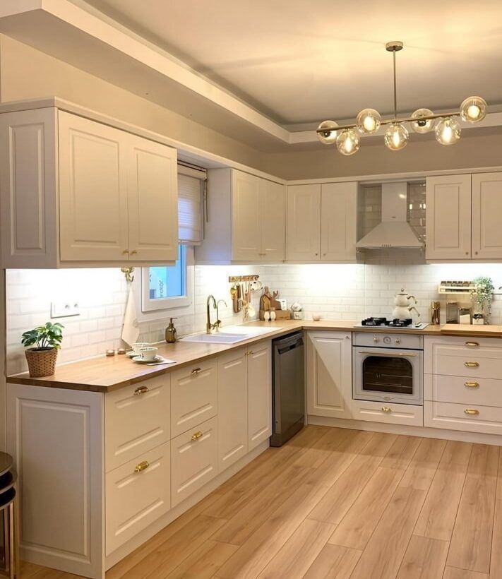 Cream-colored kitchen with wooden countertops, white cabinets, and gold hardware.