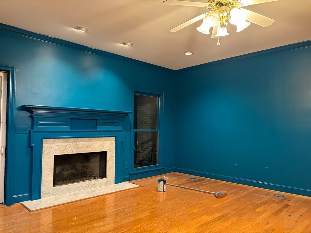 Teal living room with a fireplace, painted trim, and a ceiling fan. Wooden floors and a paint can visible.