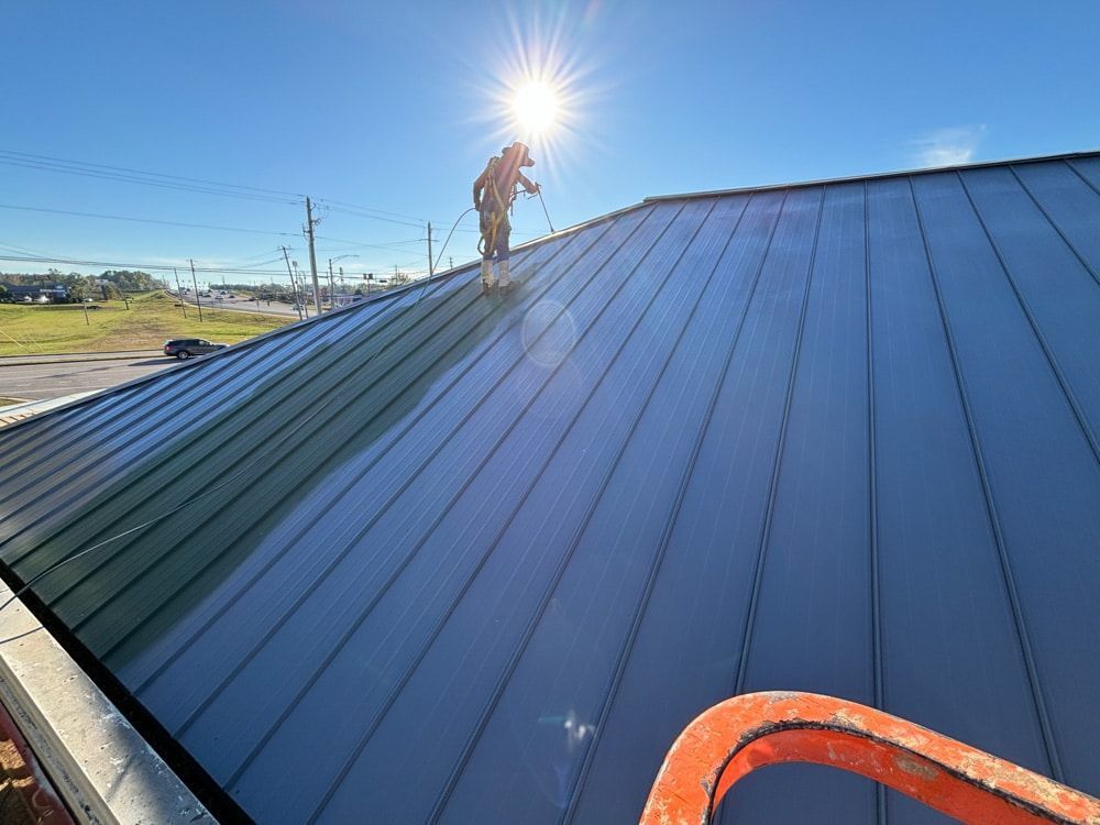Person on a metal roof spraying it, bright sun overhead.