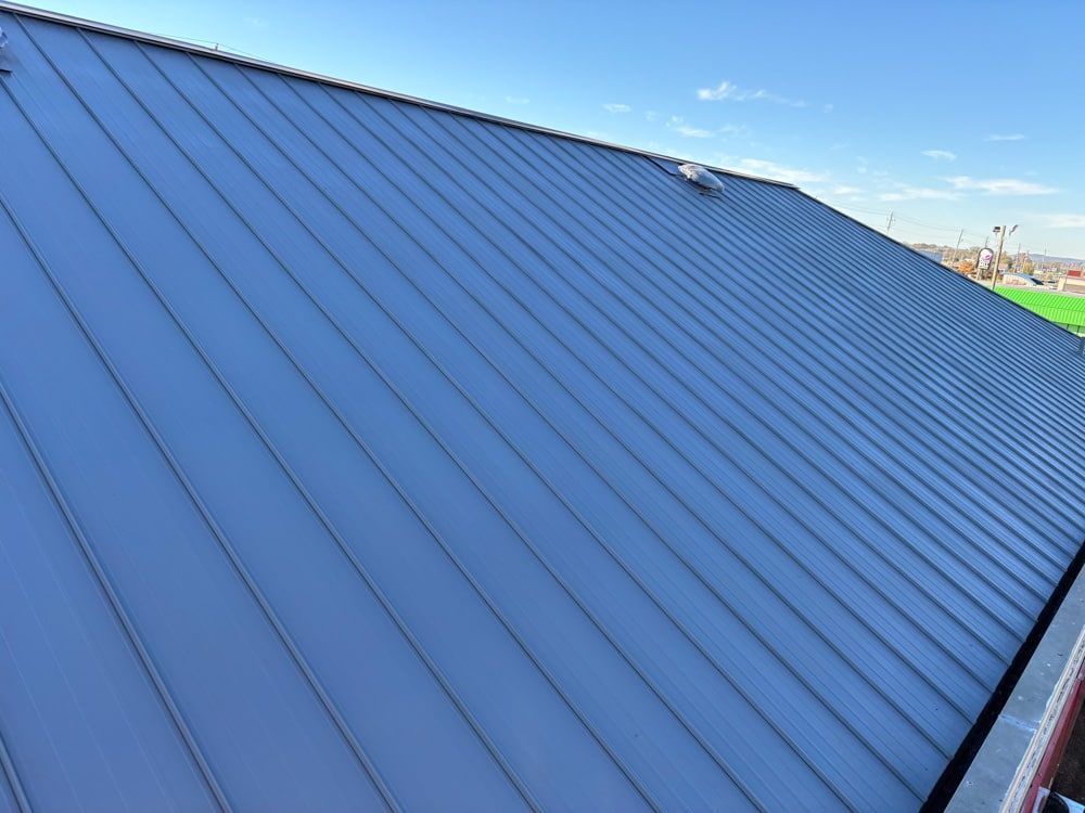 Gray metal roof with vertical seams under a blue sky.