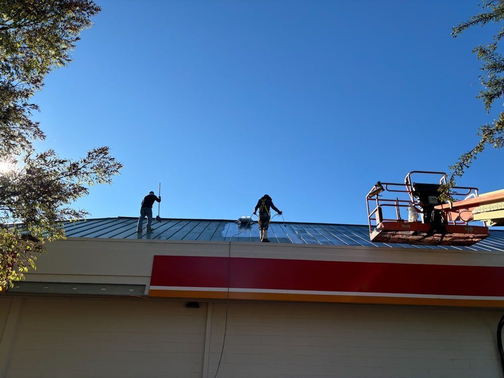 Two workers on a green metal roof, one in a lift, on a bright sunny day.