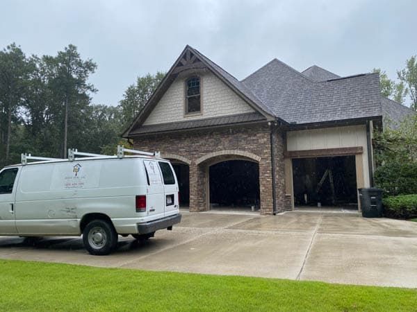 White van parked in front of a house with open garage doors; brick and brown exterior. Overcast day.
