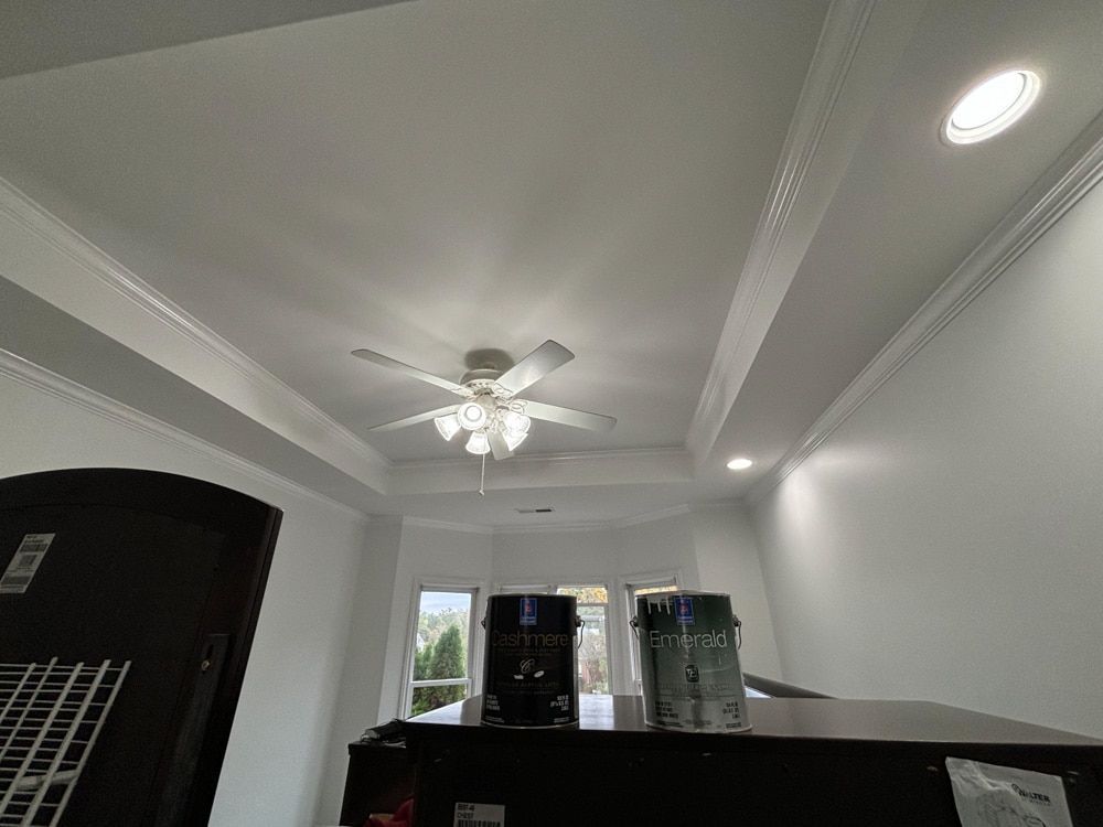 Ceiling with crown molding, ceiling fan, and recessed lighting; black furniture in front of windows.