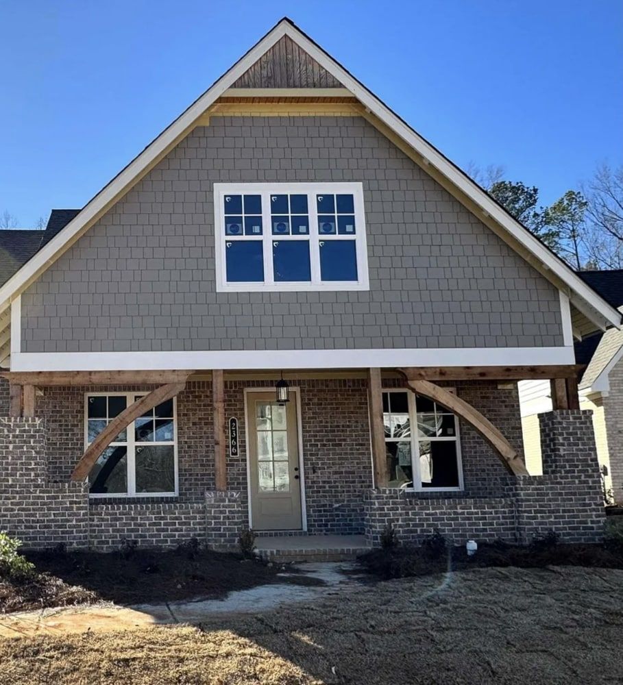 New home exterior with gray siding, brick, and arched wooden accents.