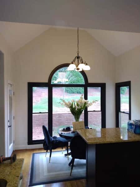 Dining area with arched window, black frames, and chandelier. Table with flowers, chairs, and a granite countertop.