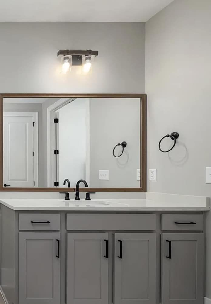 Bathroom with gray cabinets, white countertop, large mirror, and black fixtures.